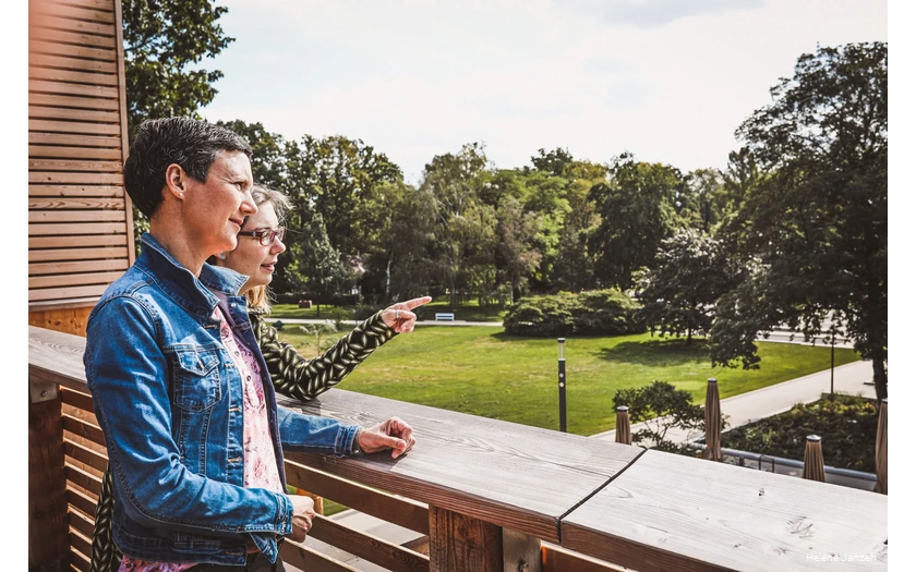 Zwei Frauen stehen auf der Terrasse des Gradierwerks und schauen auf den Kurpark. Die eine Frau zeigt mit dem Finger auf etwas und erzählt der anderen Frau etwas.