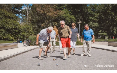 Eine Gruppe Boulespieler (4 Männer und 3 Frauen) auf dem Boulefeld im Kurpark, stehen um ihre geworfenen Boulekugeln herum und erörtern die Ergebnisse.
