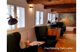 Arrangement aus grünen Armlehnensesseln und Holztischen, auf denen die Zeitungen zum Lesen ausliegen.