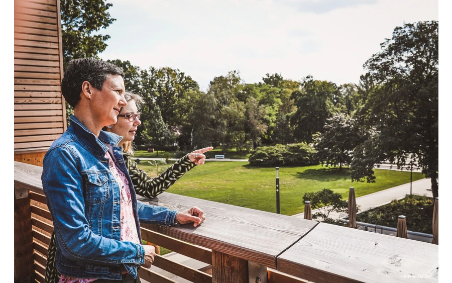 Zwei Frauen stehen auf der Terrasse des Gradierwerks und schauen auf den Kurpark. Die eine Frau zeigt mit dem Finger auf etwas und erzählt der anderen Frau etwas.