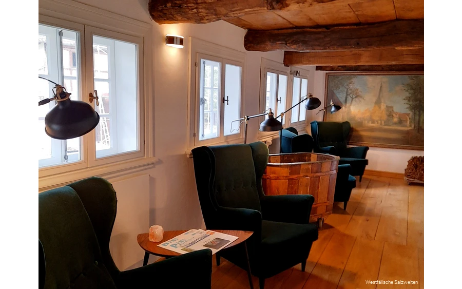 Arrangement aus grünen Armlehnensesseln und Holztischen, auf denen die Zeitungen zum Lesen ausliegen.