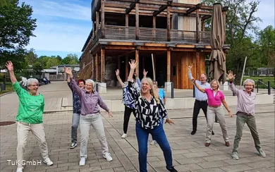 Eine Gruppe unterschiedlicher Menschen tanzt im Kurpark Bad Sassendorf. Alle haben Spaß dabei und lachen.