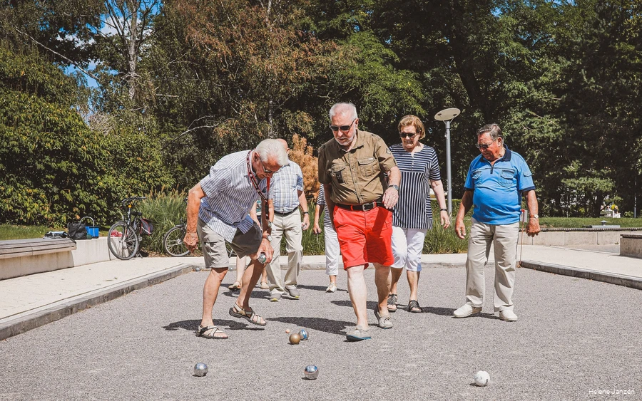 Eine Gruppe Boulespieler (4 Männer und 3 Frauen) auf dem Boulefeld im Kurpark, stehen um ihre geworfenen Boulekugeln herum und erörtern die Ergebnisse.