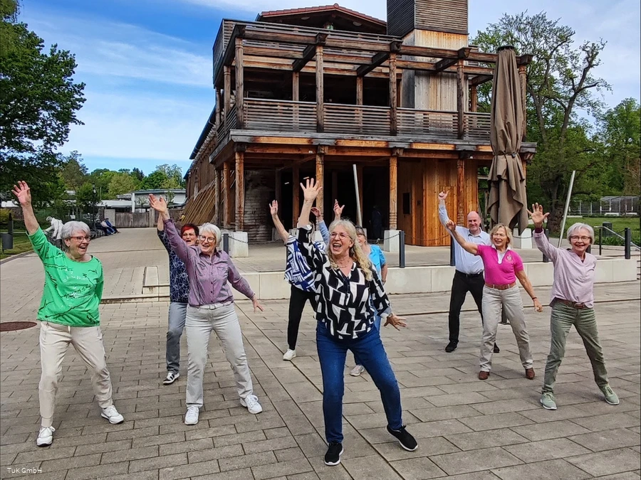 Eine Gruppe unterschiedlicher Menschen tanzt im Kurpark Bad Sassendorf. Alle haben Spaß dabei und lachen.